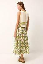 Woman wearing a white sleeveless top with green stripes and a green floral skirt on a white background