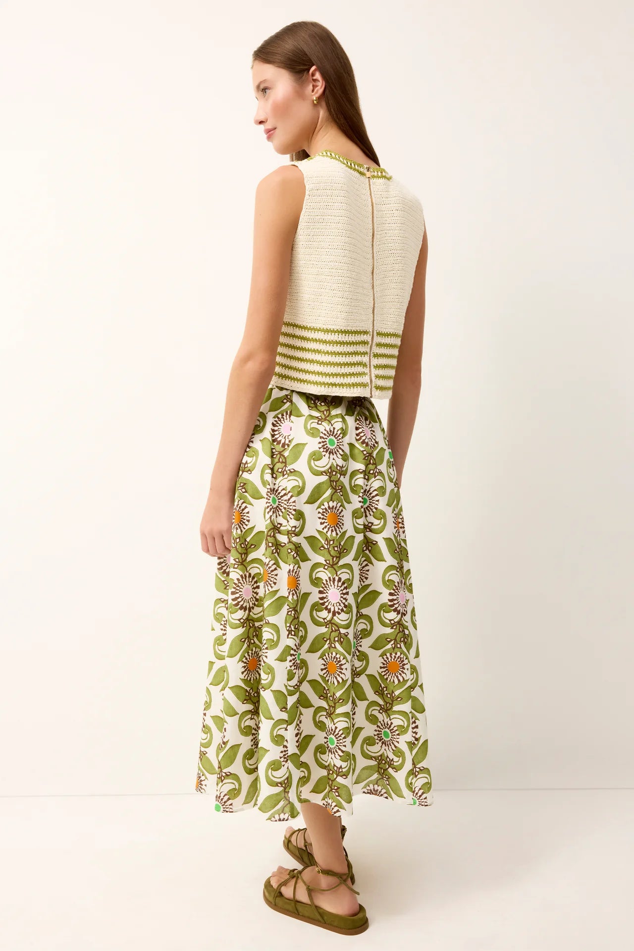 Woman wearing a white sleeveless top with green stripes and a green floral skirt on a white background