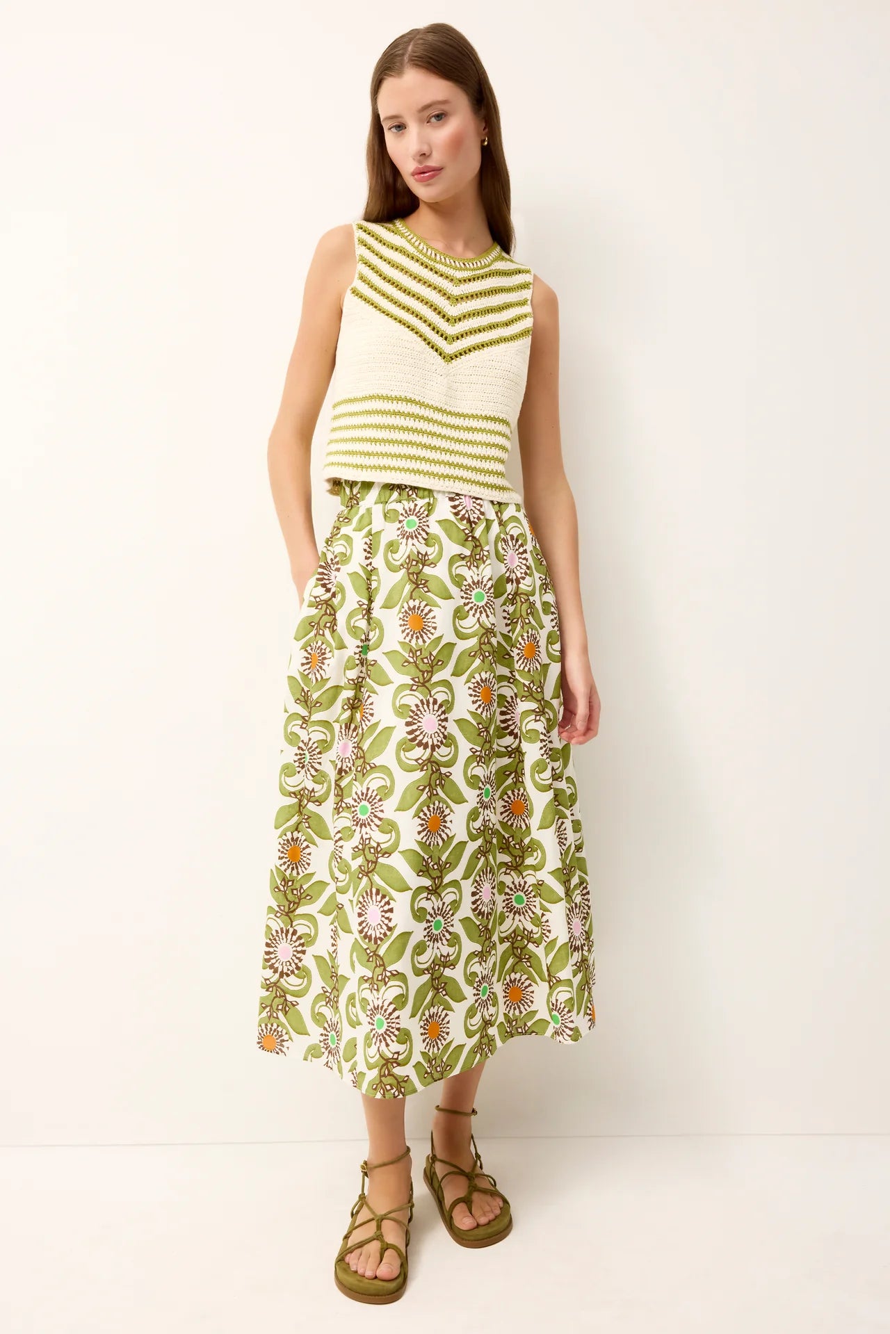 Woman wearing a green and white striped sleeveless top with a floral skirt on a white background