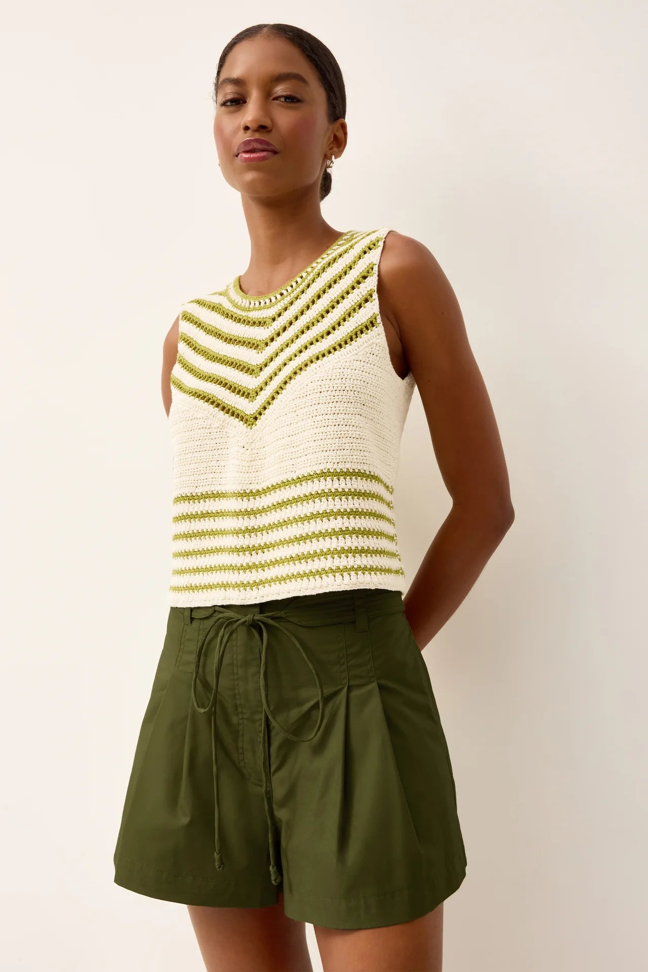 Woman wearing a white and green striped sleeveless top with green shorts against a plain background