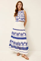 Woman wearing a white dress with blue floral patterns on a plain background