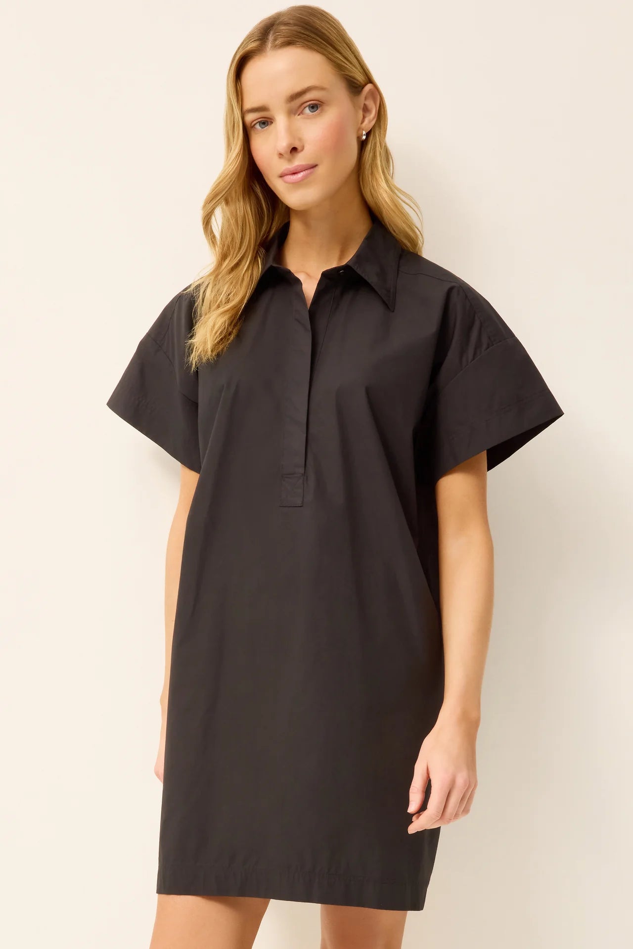 Woman wearing a black dress with short sleeves against a plain background