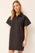 Woman wearing a black dress with short sleeves against a plain background