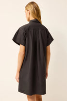 Woman wearing a black shirt dress against a plain background