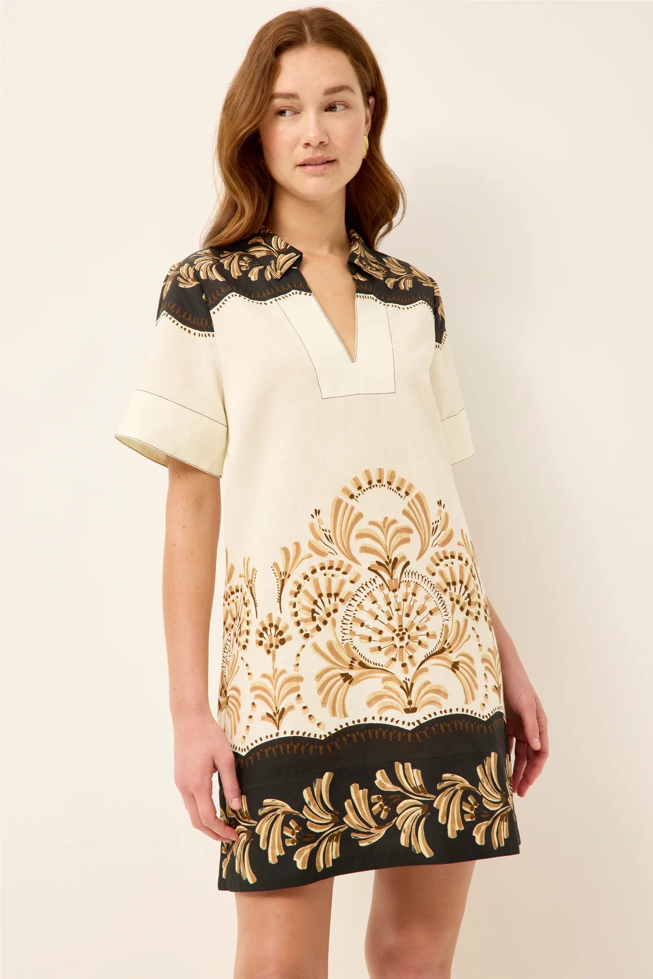 Woman wearing a cream dress with black and gold floral patterns on a white background
