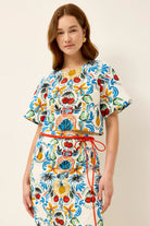 Woman wearing a colorful patterned dress with a red belt on a beige background