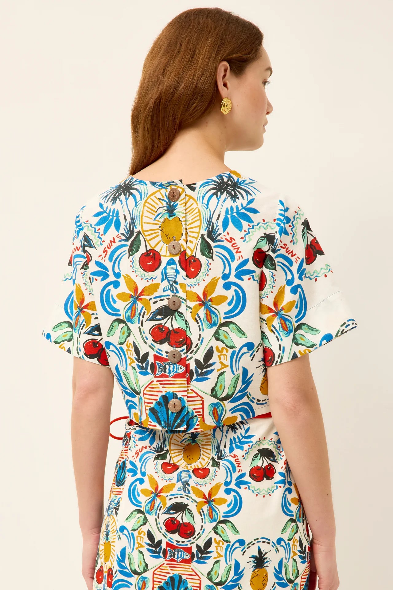 Woman wearing a colorful patterned dress with a red belt on a beige background