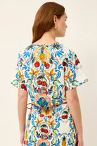 Woman wearing a colorful patterned dress with a red belt on a beige background