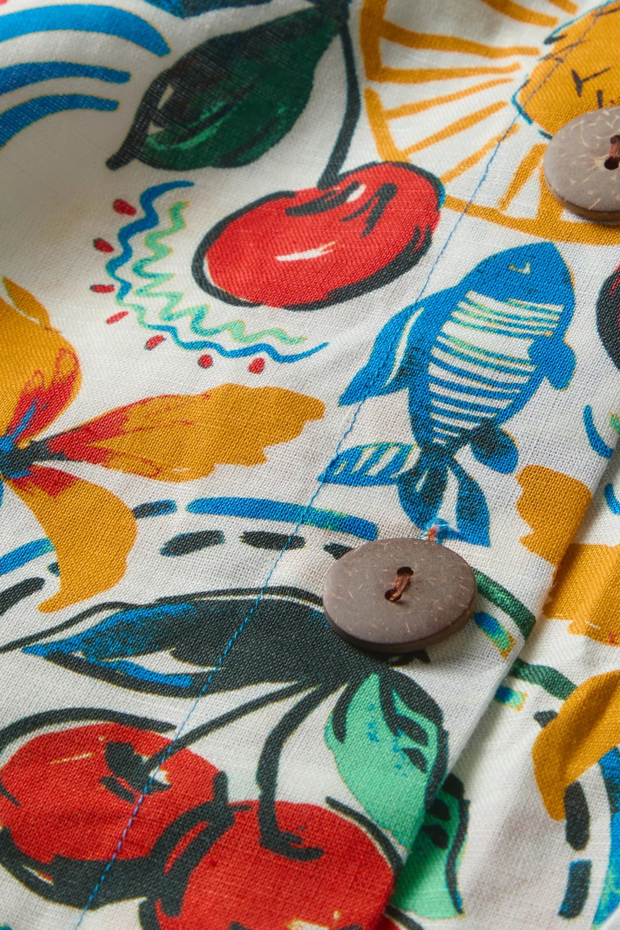Close-up of a colorful fabric with fish, cherry, and leaf patterns.