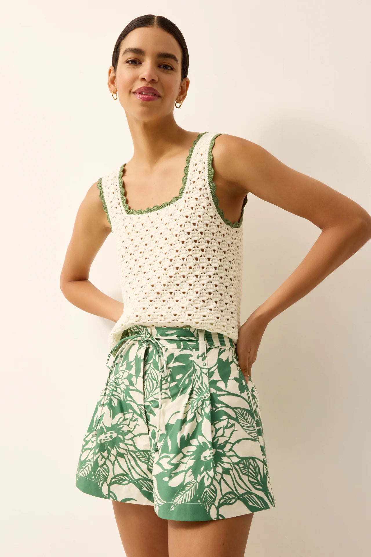 Woman wearing a white crochet top and green floral shorts against a plain background
