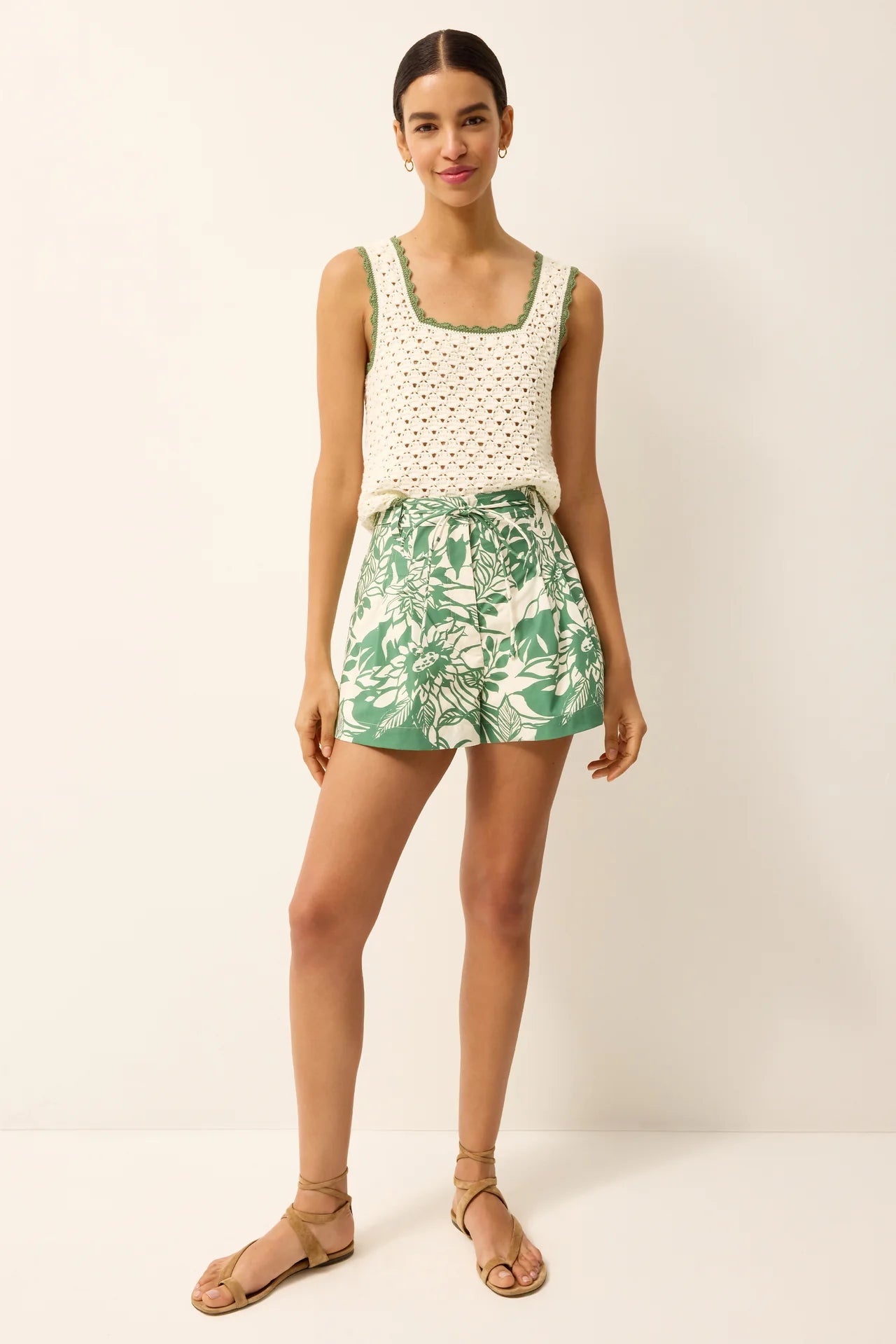 Woman wearing a white sleeveless top with a green leaf patterned skirt on a plain background