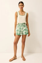 Woman wearing a white sleeveless top with a green leaf patterned skirt on a plain background