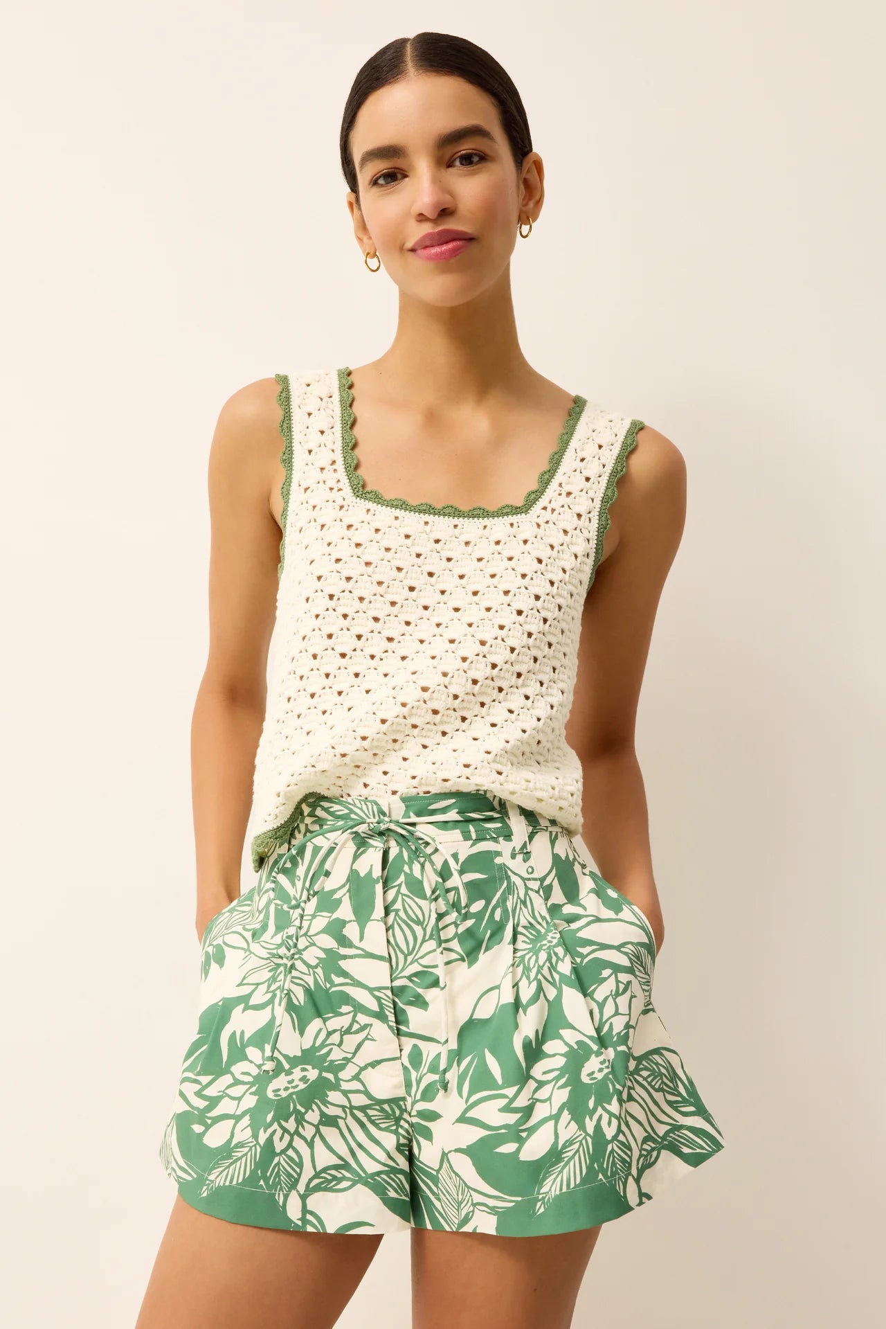 Woman wearing a white top with green trim and green floral shorts on a plain background