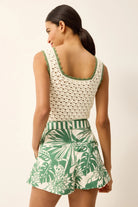 Woman wearing a white top with green trim and a green and white patterned skirt on a beige background