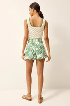 Woman wearing a sleeveless top and leaf-patterned shorts on a white background