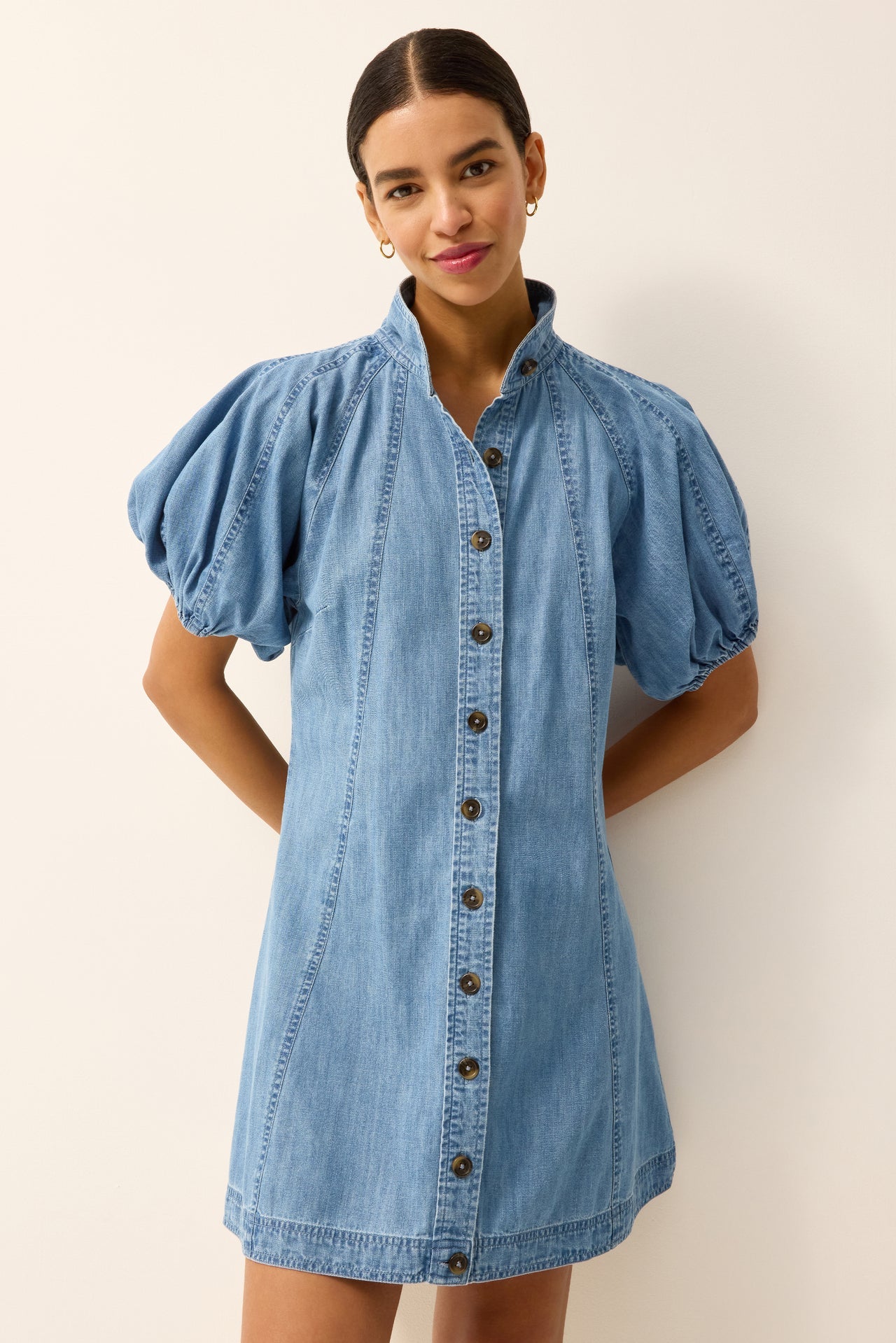 Woman wearing a denim dress with puff sleeves against a plain background