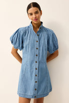 Woman wearing a denim dress with puff sleeves against a plain background