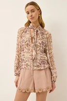 Woman wearing a floral blouse and beige shorts on a plain background