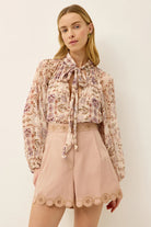 Woman wearing a floral blouse and pink shorts against a white background