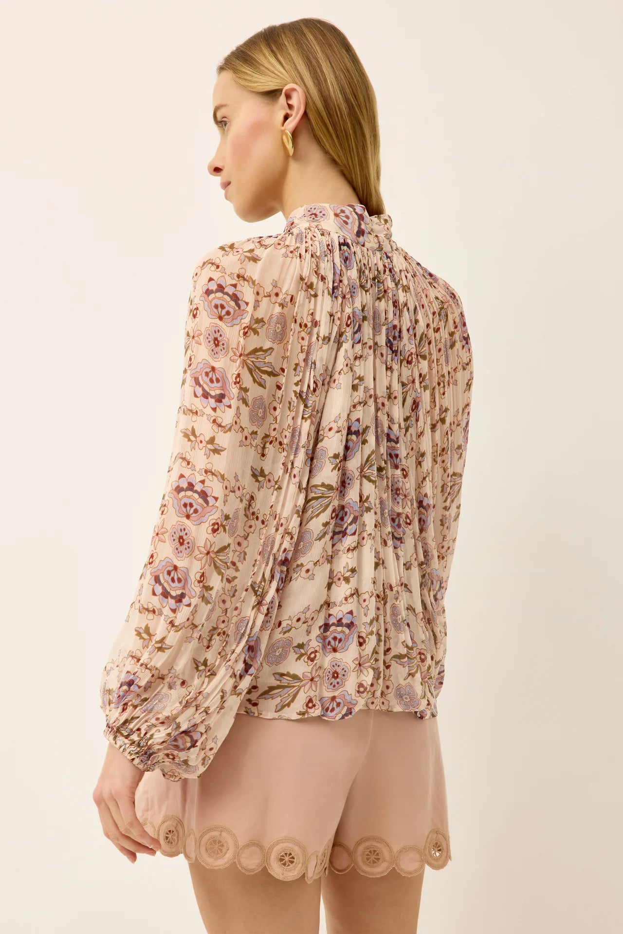 Woman wearing a floral blouse with sheer sleeves on a beige background