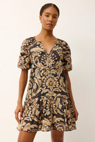Woman wearing a black and gold floral patterned dress on a white background