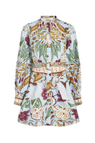 A long-sleeve tunic dress with a high mock neck, featuring an all-over botanical and abstract pattern in green, burgundy, gold, and cream on a light blue base, complete with a matching fabric belt.
