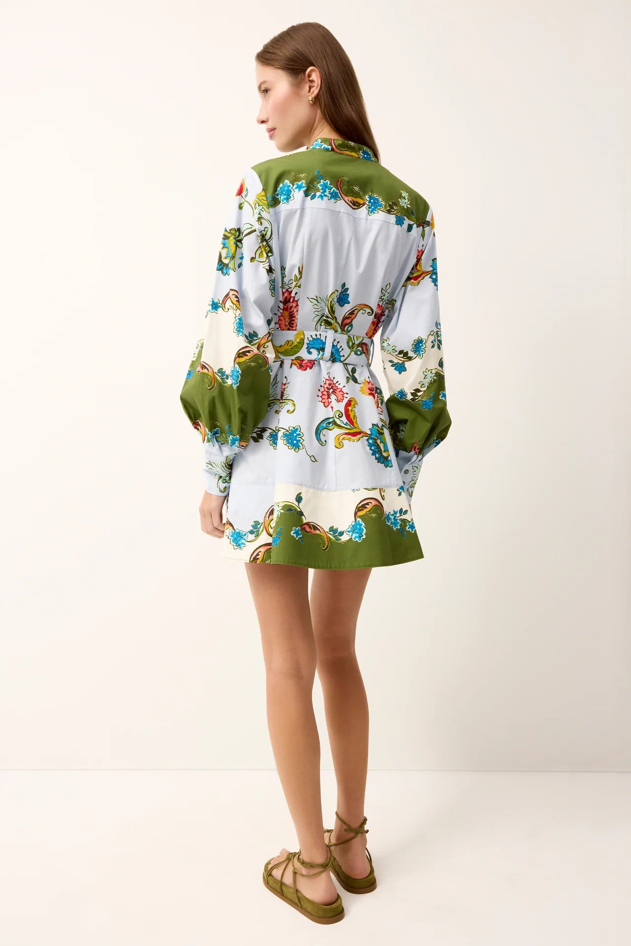 Woman wearing a colorful floral dress with a green jacket on a white background