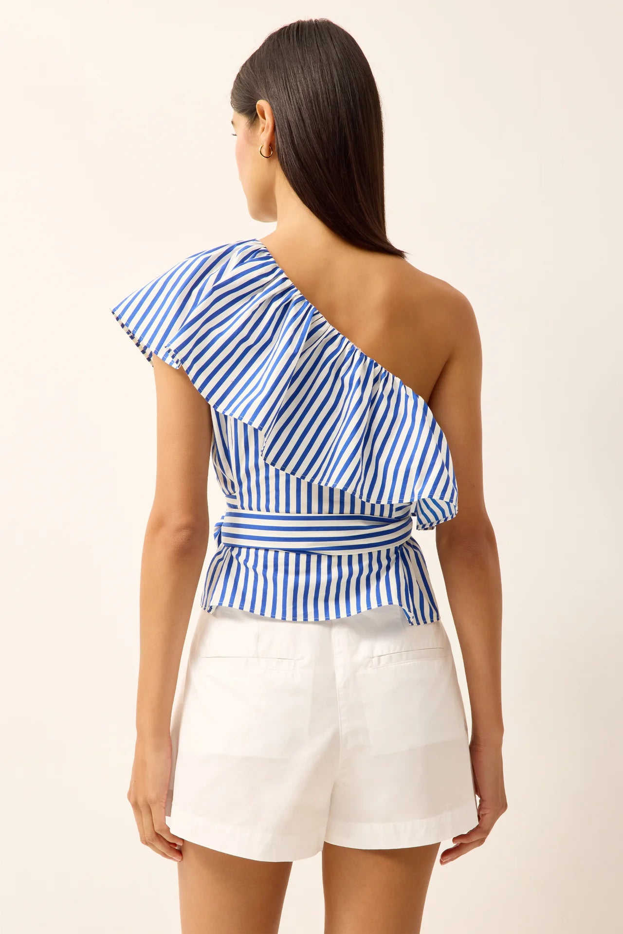 Woman wearing a blue and white striped one-shoulder top and white shorts against a white background