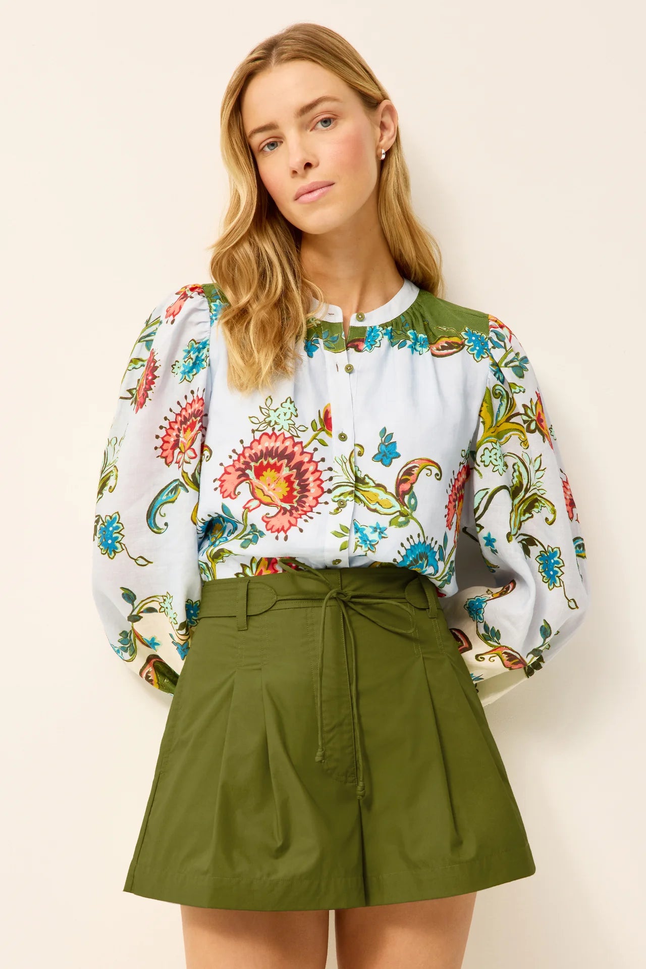 Woman wearing a floral blouse and green skirt against a plain background