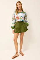 Woman wearing a floral blouse and green shorts on a white background