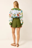 Woman wearing a floral blouse and green shorts on a white background