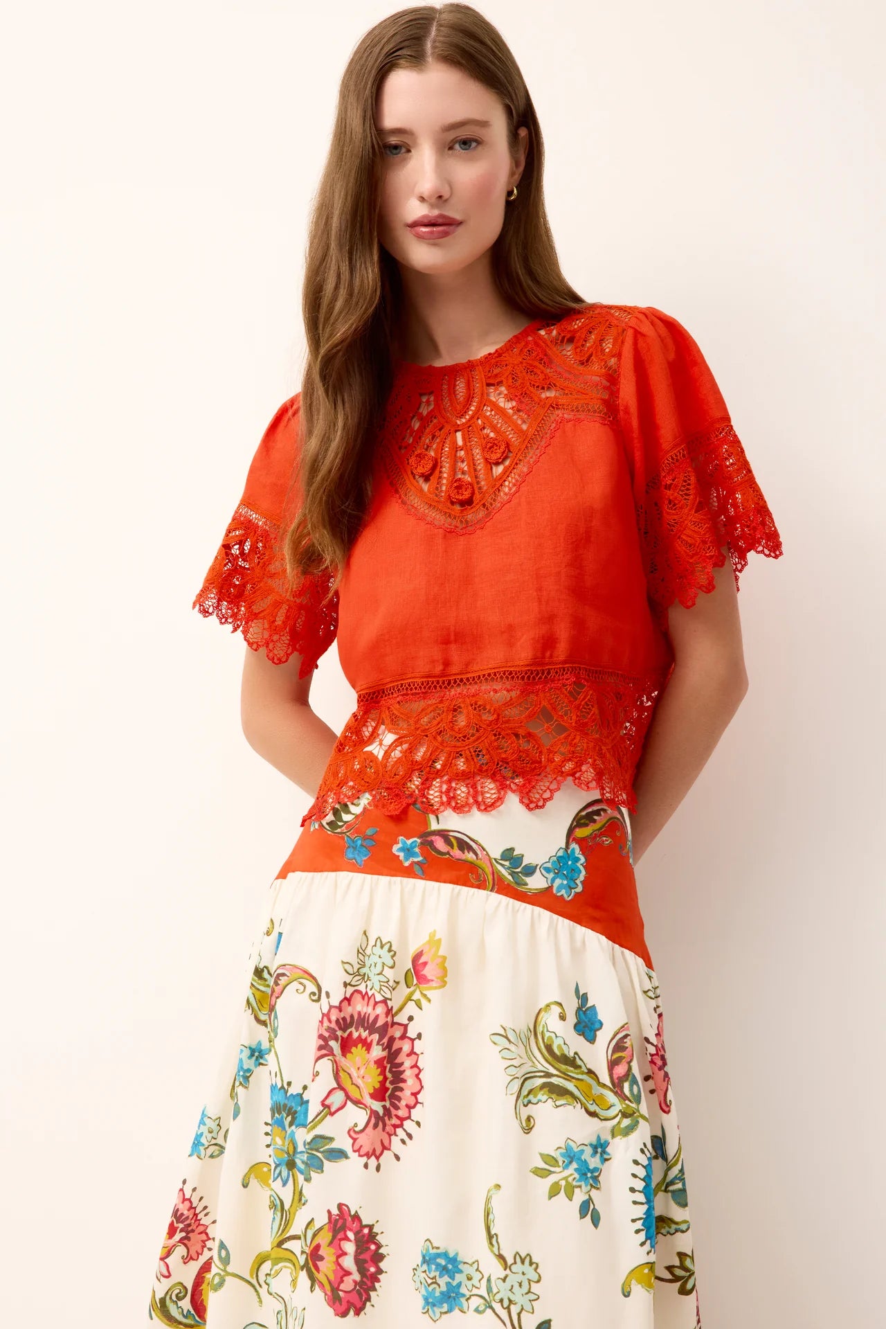 Woman wearing a red embroidered top and white floral skirt on a white background