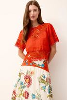 Woman wearing a red embroidered top and white floral skirt on a white background