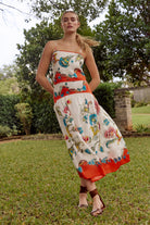 Woman wearing a colorful floral dress standing in a grassy area with trees in the background