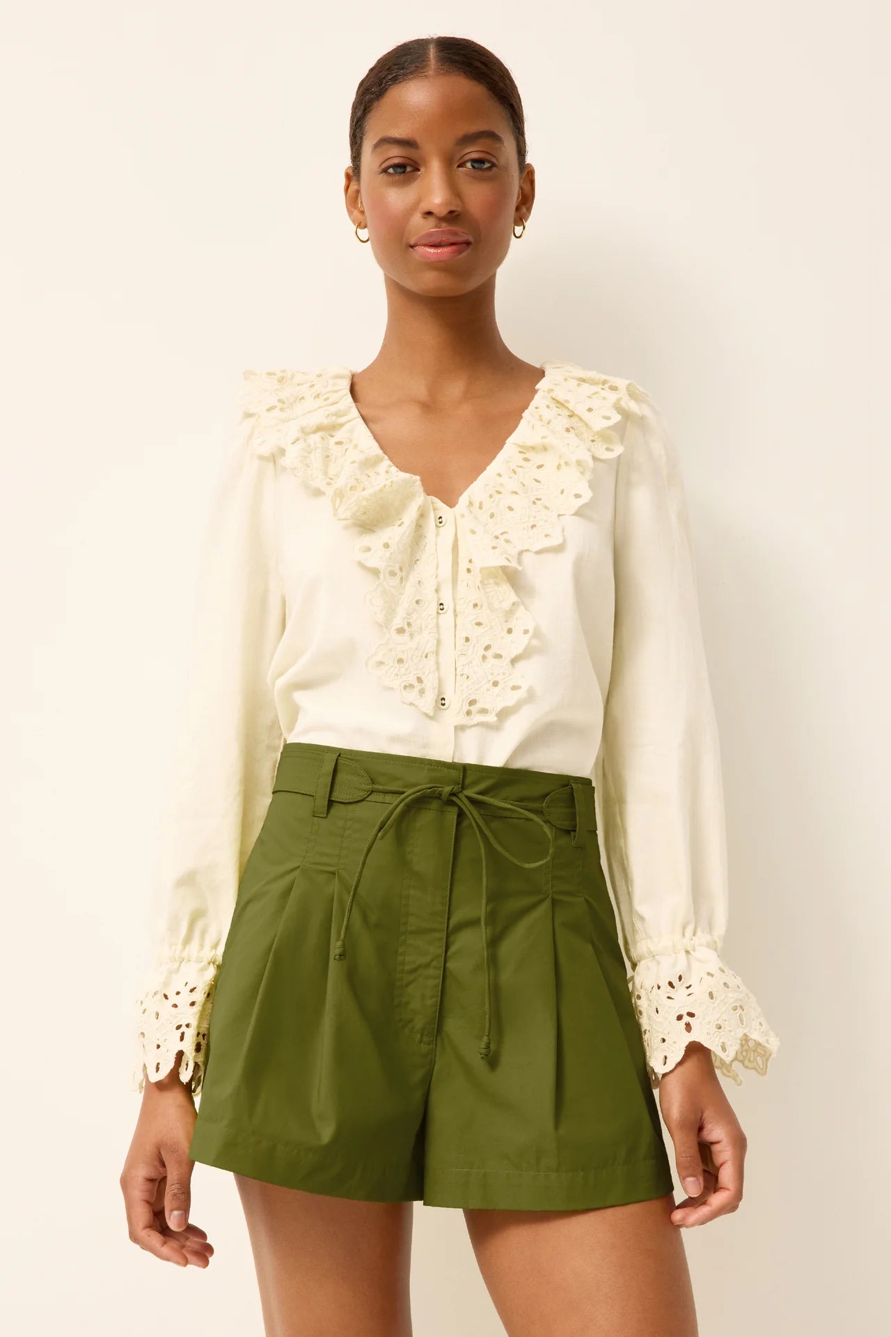 Woman wearing a white blouse with lace details and green shorts on a plain background