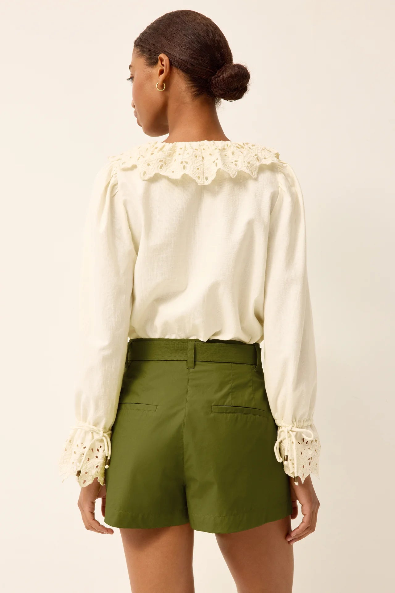 Woman wearing a white blouse with lace details and green shorts on a beige background