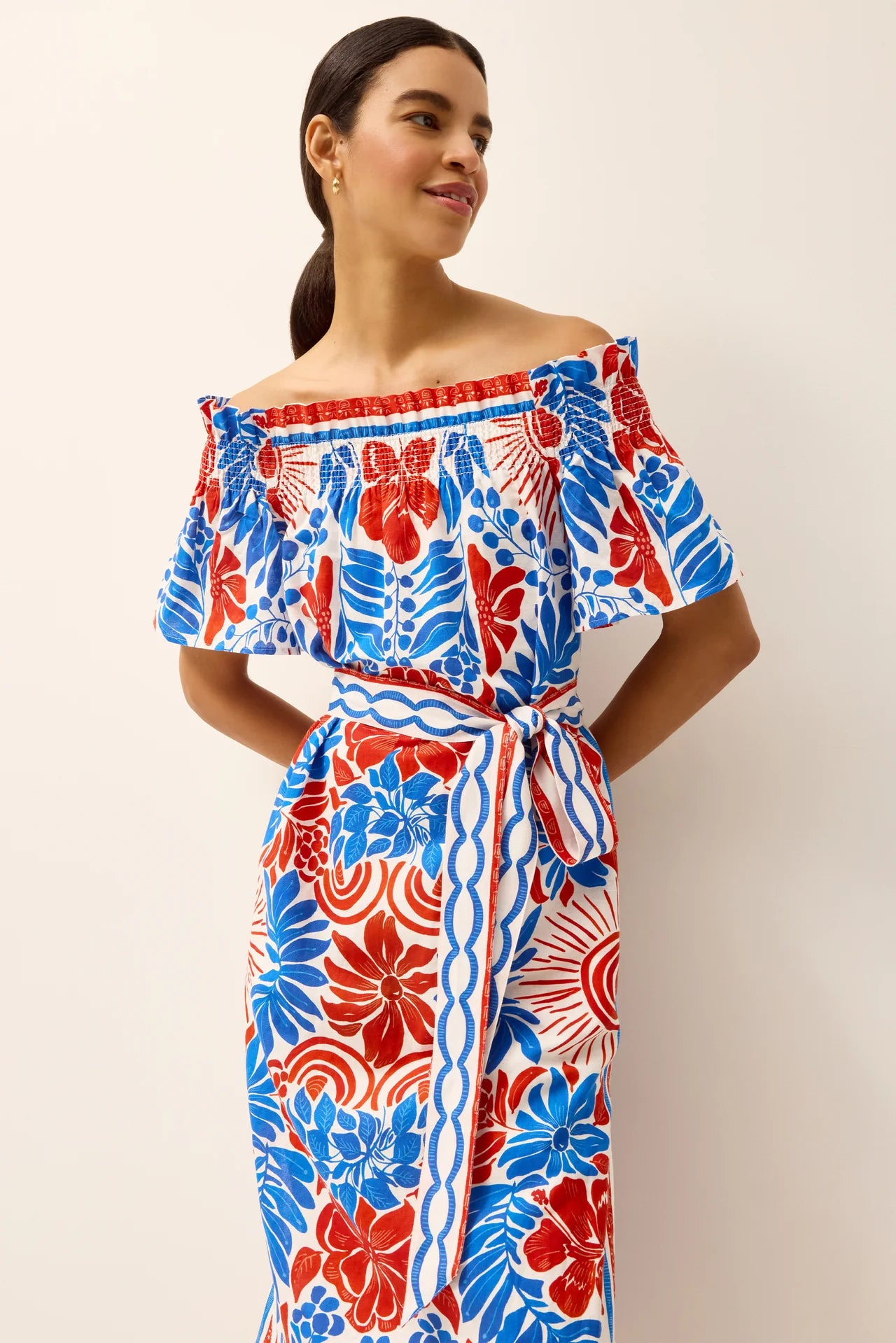 Woman wearing a red, blue, and white floral dress against a plain background