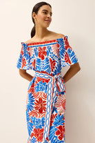 Woman wearing a red, blue, and white floral dress against a plain background