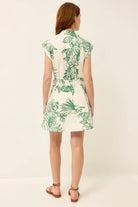 Woman wearing a white dress with green leaf pattern on a plain background
