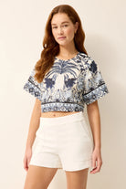 Woman wearing a patterned crop top and white shorts on a plain background