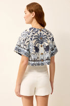 Woman wearing a patterned top and white shorts on a beige background