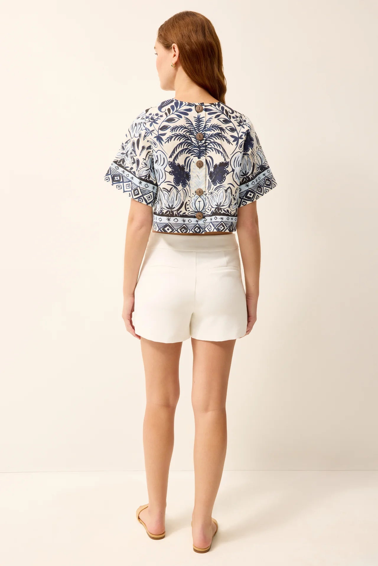 Woman wearing a patterned top and white shorts on a plain background