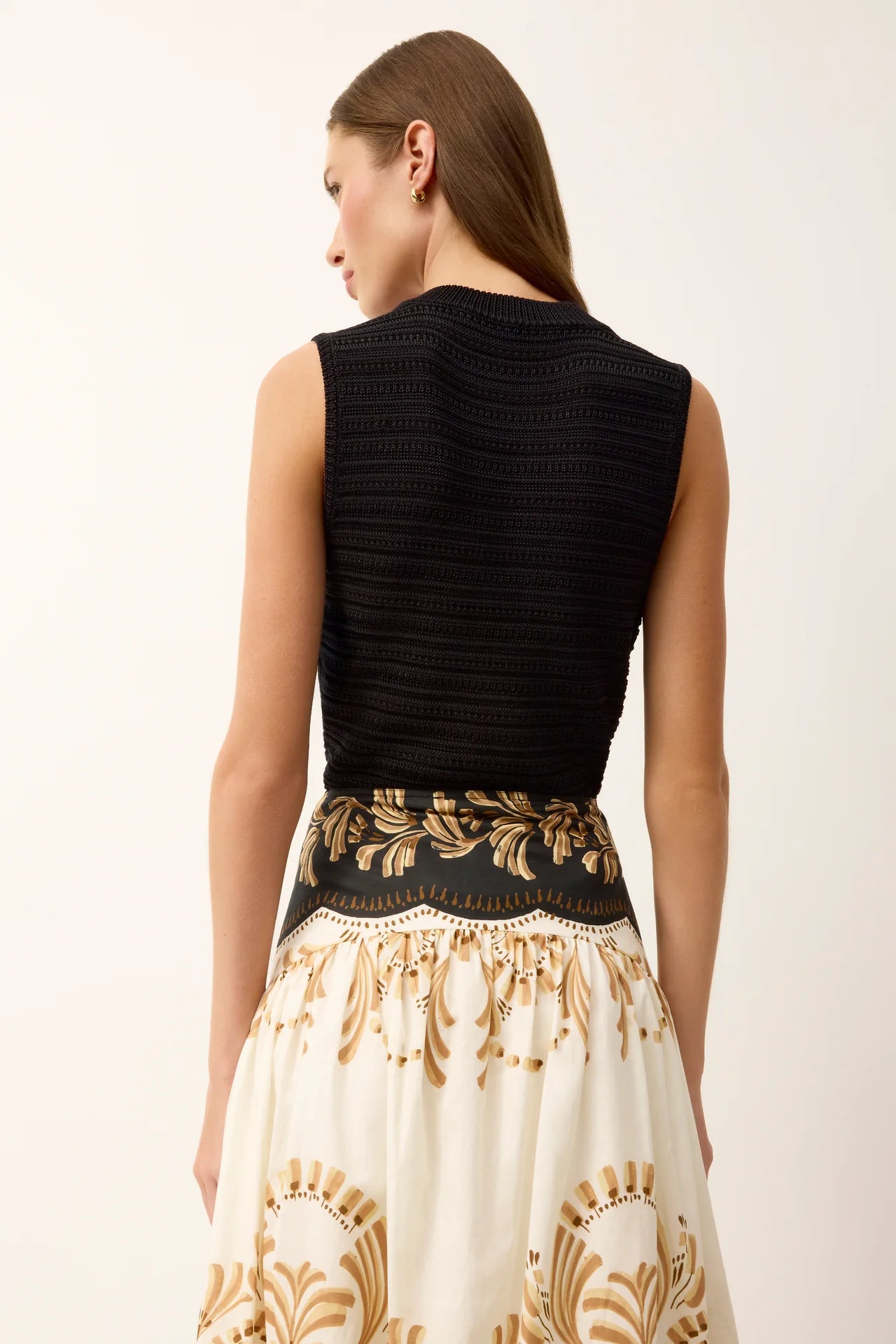 Woman wearing a black sleeveless top and patterned skirt on a white background