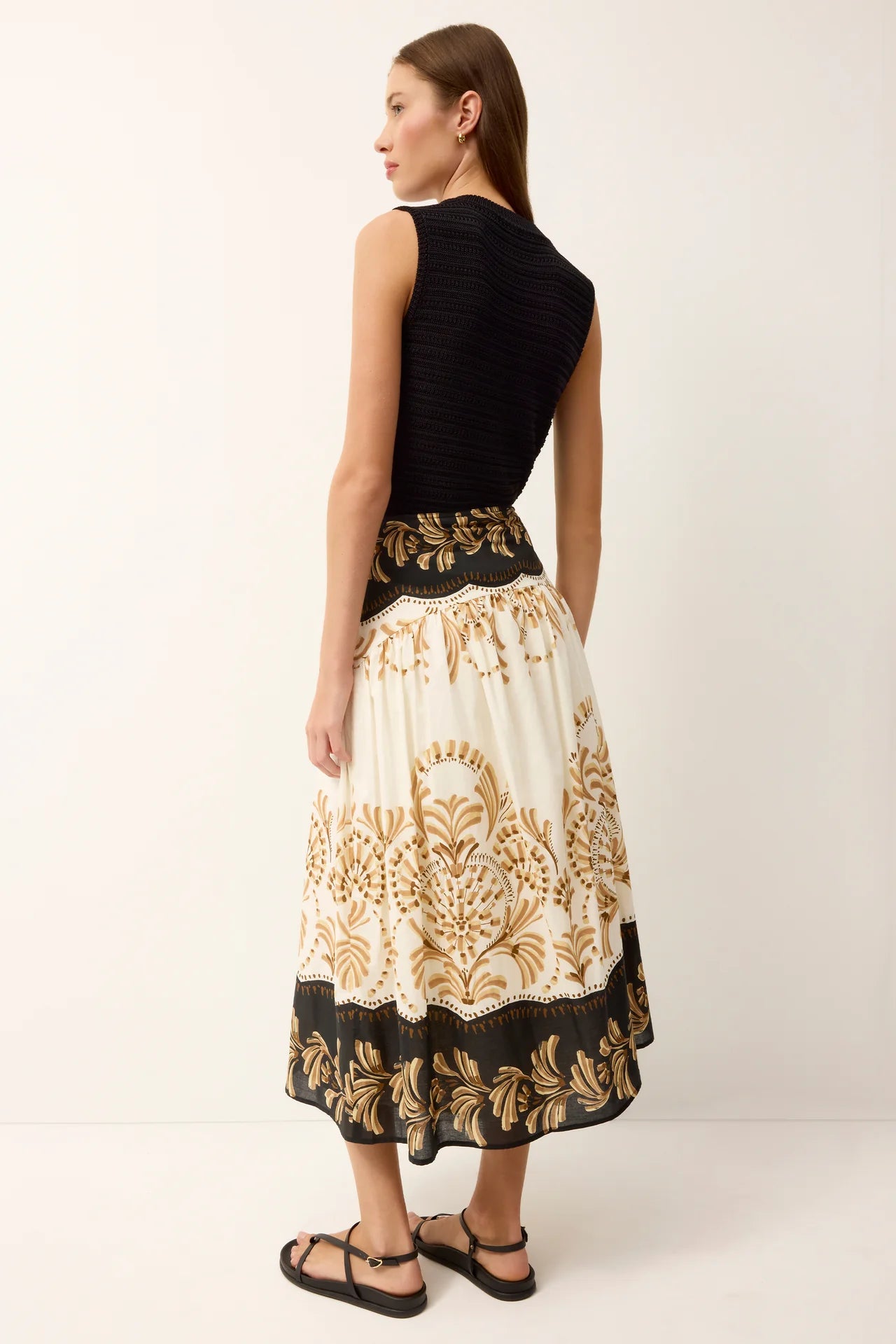 Woman wearing a black top and a long, patterned skirt on a white background