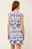 Woman wearing a white dress with blue floral patterns on a plain background