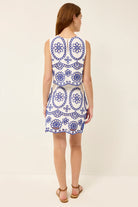 Woman wearing a white dress with blue floral patterns on a plain background