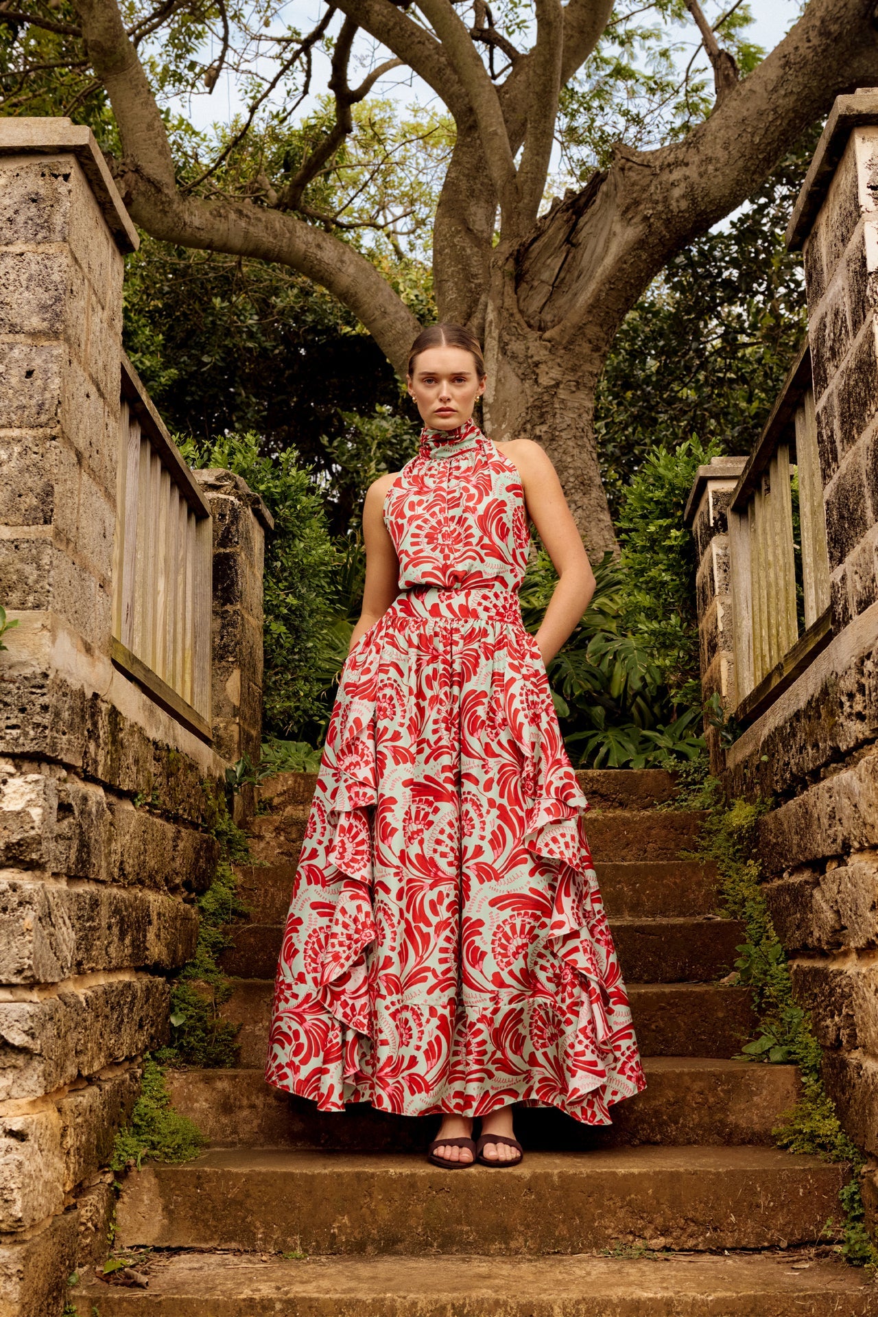 Woman in a red and white floral dress standing on stone steps with trees in the background