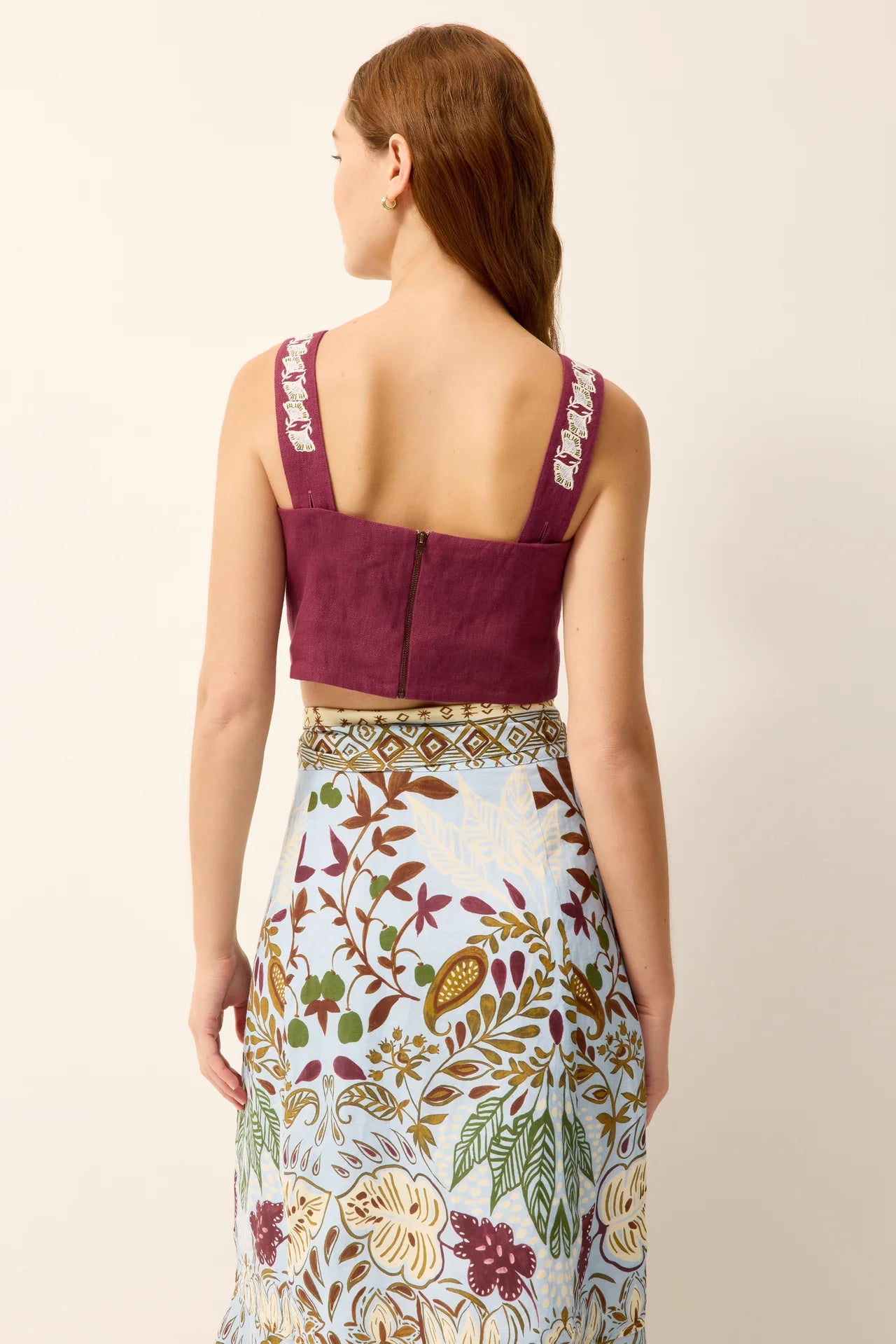 Woman wearing a maroon top and floral skirt on a beige background