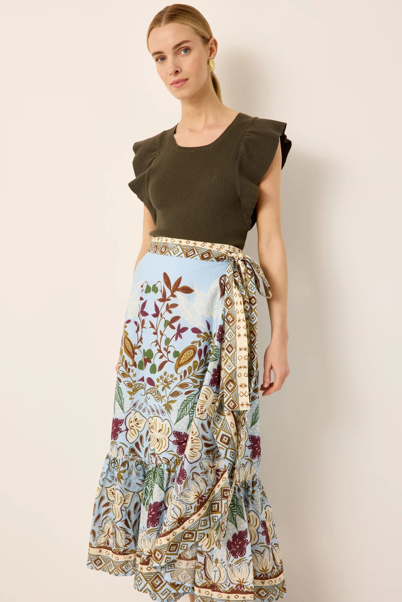 Woman wearing a green top and patterned skirt against a plain background