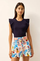 Woman wearing a navy top and colorful patterned shorts on a plain background